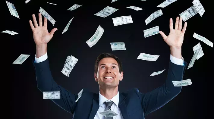 Businessman joyfully reaching for falling money, representing successful AWS cost saving strategies to reduce AWS expenses.